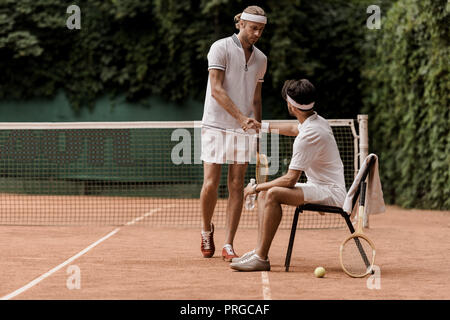 retro styled tennis players shaking hands at tennis court Stock Photo