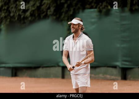 smiling handsome retro styled tennis player holding racket at court Stock Photo