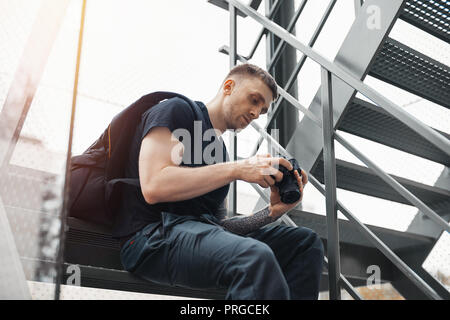 Attractive man sitting at staircase and checking photos in camera. Stock Photo