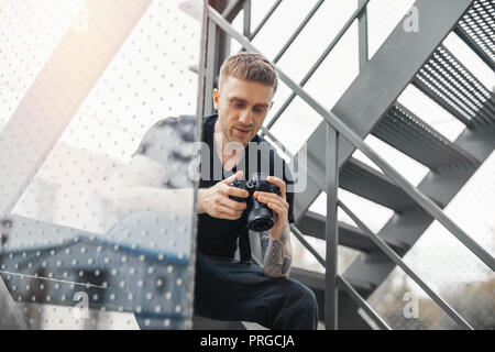 Attractive man sitting at staircase and checking photos in camera. Stock Photo