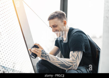 Attractive man sitting at staircase, smiling and checking photos in camera. Stock Photo