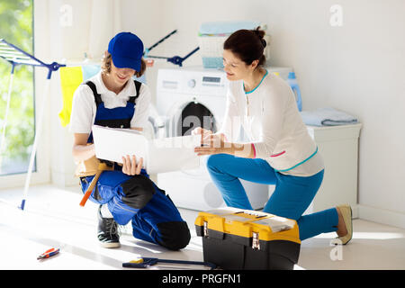 Washing machine repair service. Young technician examining and repairing tumble dryer. Woman looking at broken household appliance. Plumber with custo Stock Photo