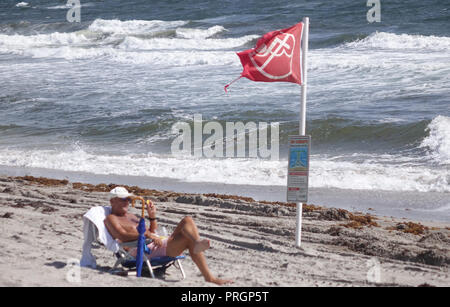 Boca Raton, Florida, USA. 2nd Oct, 2018. Richard Desmoni of Boca Raton rests near a red flag warning people of severe hazards in the water at Red Reef Park. Red tide has been confirmed in Palm Beach County. Credit: Joe Cavaretta/Sun-Sentinel/ZUMA Wire/Alamy Live News Stock Photo