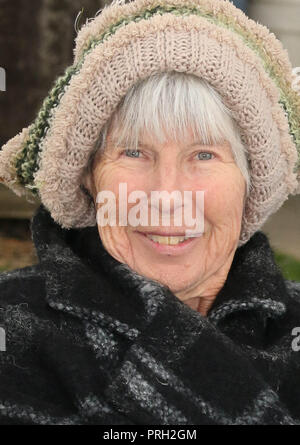 Retired lady enjoying sitting outside with winter coat and woolly hat on. Stock Photo