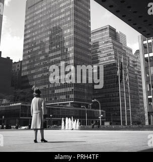 1960s, historical, a lady in coat and with handbag looking up at the large modern glass buildings and skyscapers dominating the Manhattan skyline in New York city, New York, USA. Stock Photo