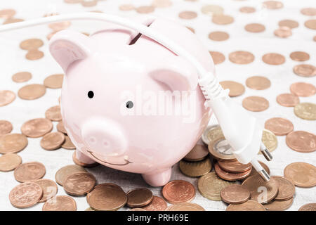 Electric Cable Lying On A Piggybank Surrounded By Coins - Saving Money By Reducing Power Consumption Concept Stock Photo