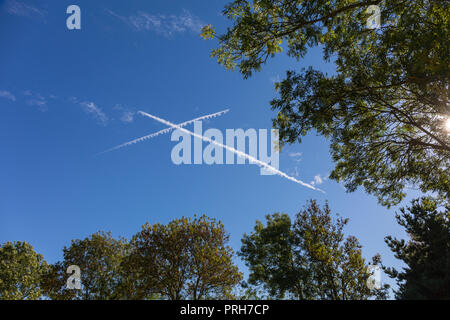 Vapour trails from two aeroplanes make an X cross in a blue sky over Suffolk, UK. Stock Photo
