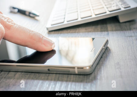 Finger Touching Mobile Phone With Reflection Next To A White Keyboard And A Biro On A Table - Office Meeting Concept Stock Photo