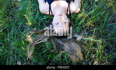 portrait young blonde woman laying in the grass with long hair and blue eyes