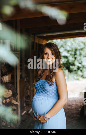 portrait of beautiful pregnant woman in blue dress holding her belly and smiling into the camera Stock Photo