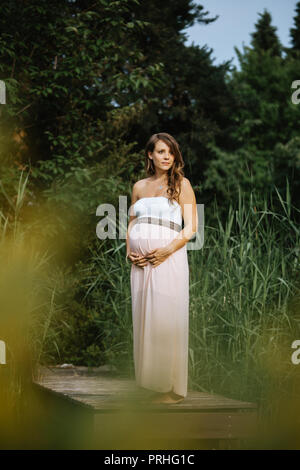 portrait of beautiful pregnant woman standing at a lake looking straight ahead Stock Photo