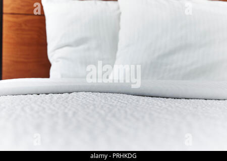 Folded white bed covers and pillows on a made bed with shallow depth of field Stock Photo