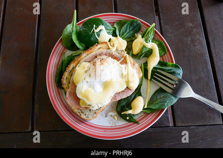 Eggs Benedict served on a plate with spinach salad, bacon rasher, a piece of toast and sauce hollandaise Stock Photo