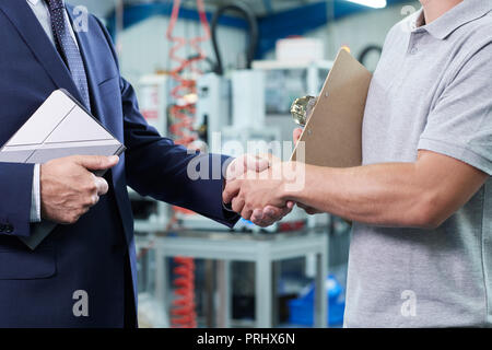 Close Up Of Business Owner With Digital Tablet In Factory Shaking Hands With Engineer Stock Photo
