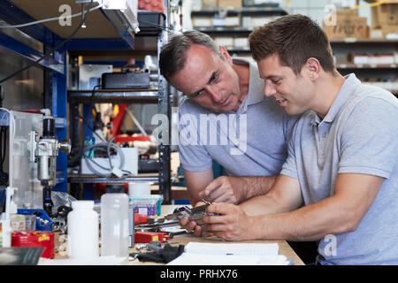 Engineer Helping Male Apprentice In Factory To Measure Component Using Micrometer Stock Photo