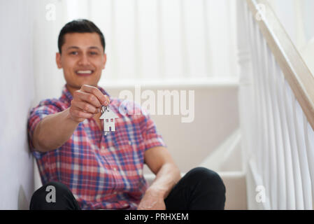 Young Man Sitting On Stairs Holding Keys To New Home Stock Photo