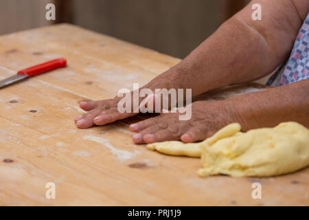 A typical orecchiette lady from the italian city Bari is kneading the dough on a wooden table to make pasta Stock Photo