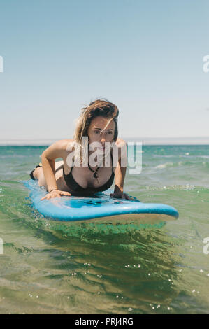 young woman in bikini lying on surfing board in ocean Stock Photo