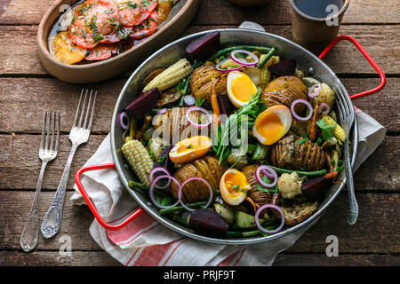 Homemade Hasselback Potatoes in a pat with root vegetables. Stock Photo