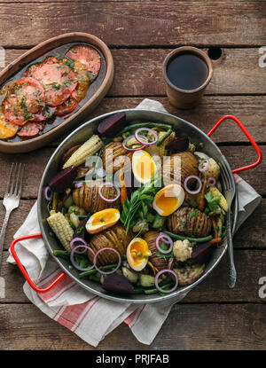 Homemade Hasselback Potatoes in a pat with root vegetables. Stock Photo