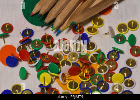 Thumbtacks and colored pencils scattered on a colored plane, horizontal image Stock Photo
