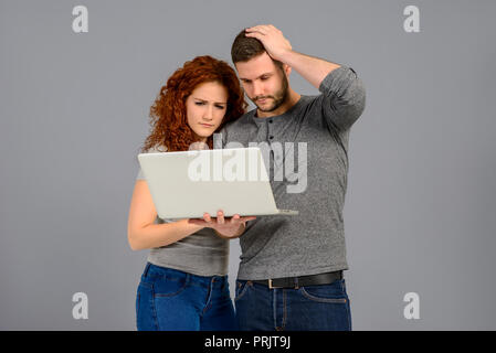 A handsome young man holding a laptop next to his girlfriend and they both feeling upset Stock Photo