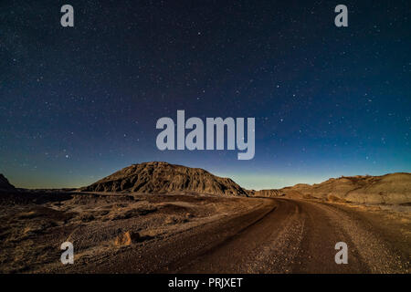 A moonlit nightscape of the badlands loop road in Dinosaur Provincial Park, arcing off toward the Big Dipper in the northern sky. Vega is setting at f Stock Photo