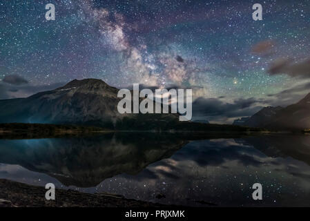 The Milky Way reflected in the unusually calm waters of Middle Waterton Lake from Driftwood Beach, in Waterton Lakes National Park, Alberta, Canada. T Stock Photo