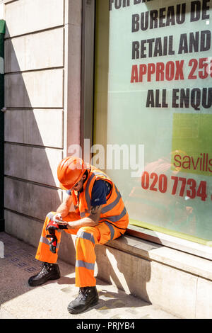 London England,UK,West End City Westminster Mayfair,man men male,worker,laborer,sitting on window ledge,hard hat,reflective vest,pants,construction sa Stock Photo