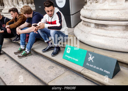 London England,UK,Bloomsbury,The British Museum,human culture history,exterior,courtyard,entrance,ionic column,man men male,young adult,sitting on ste Stock Photo