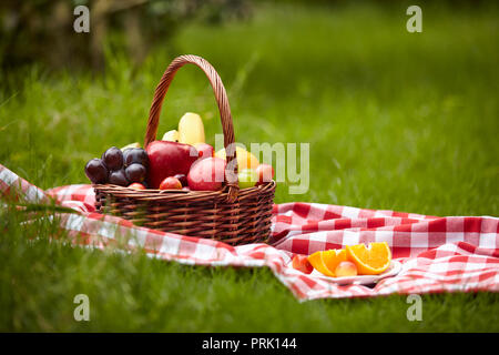 assorted fruits in a basket for picnic on grass. Stock Photo