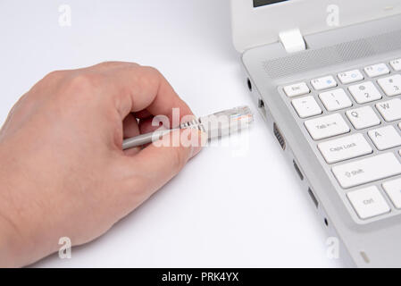 Closeup hand connection cable network connection to a Lan port of a laptop on white table, concept computer connection. Stock Photo