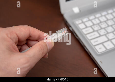 Closeup hand connection cable network connection to a Lan port of a laptop on wooden table, concept computer connection. Stock Photo