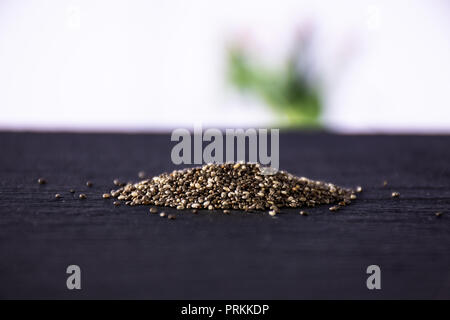 Lot of whole fresh mottled chia seeds with red flowers on white in background Stock Photo