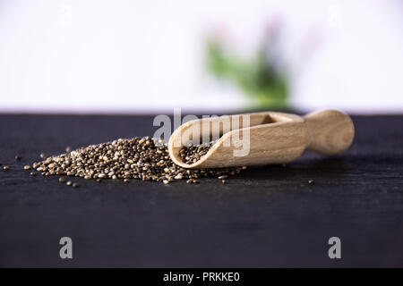 Lot of whole fresh mottled chia seeds with wooden scoop with red flowers on white in background Stock Photo