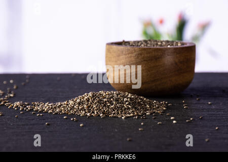 Lot of whole fresh mottled chia seeds with wooden bowl with red flowers on white in background Stock Photo