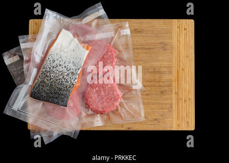 Salmon and beef burger patties vacuum packed for sous-vide cooking to be immersed in water or ready to be frozen for storage on a wooden chopping boar Stock Photo