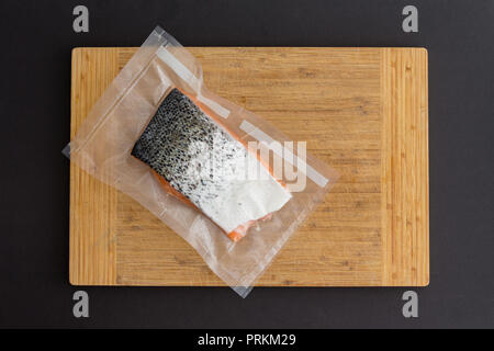Portion of gourmet fresh Atlantic salmon in a vacuum pack of clear plastic ready fro freezing lying on a bamboo board over a black background Stock Photo