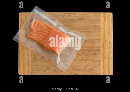 Piece of gourmet oceanic salmon vacuum packed in clear plastic ready for freezing lying on a wooden board over black viewed from above Stock Photo