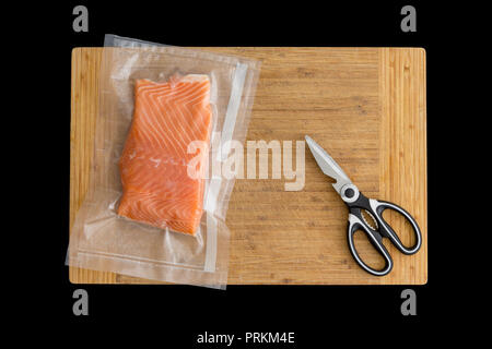 Fillet of fresh Atlantic salmon packaged fro freezing in a vacuum pack of clear plastic lying on a wooden board with scissors viewed from above Stock Photo