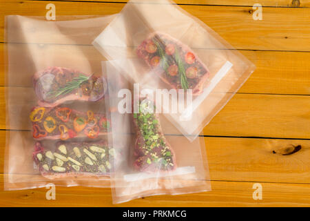 Multiple random meat dishes with bits of vegetables inside plastic bags sitting on wooden plank table Stock Photo