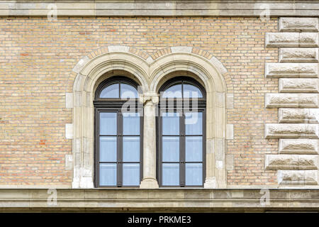 Two Windows with arches on top separated by a column with stucco on the background of a wall of beige brick. Stock Photo