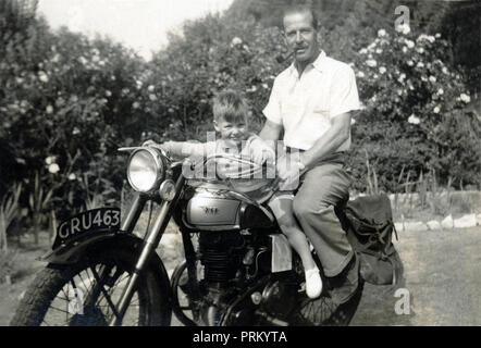 Father & young son pose for a photograph on a vintage BSA motorcycle in the back garden in the 1950s Stock Photo