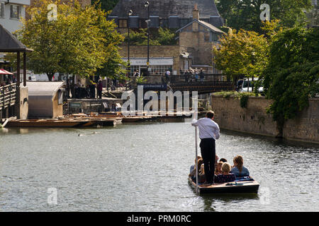 A punt boat with several people aboard on the river Cam heading to Magdalene Bridge on a sunny Summer afternoon, Cambridge, UK