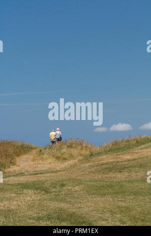 Rear view of retired couple walking beside the seaside in Cornwall, UK. Walking in UK countryside concept, country walks, couple walking away. Stock Photo