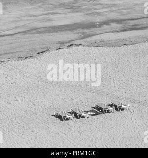 Four deserted sun-loungers on open stretch of sandy beach. On holiday concept, sun lounger towel war, & no German towels idiom, Brit German towel war. Stock Photo