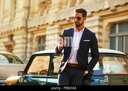 A handsome young businessman standing next to his car and using his phone Stock Photo