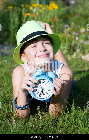 Dreams. Boy in hat laying with alarm clock in summer garden Stock Photo
