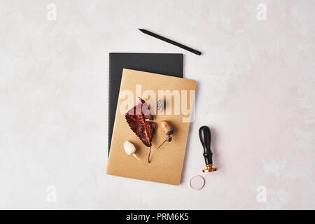 Autumn concept of the office. Top view of twok notebooks with leaf, acorn, wax seal stamp and black pencil on rose and white background. Flat lay with Stock Photo