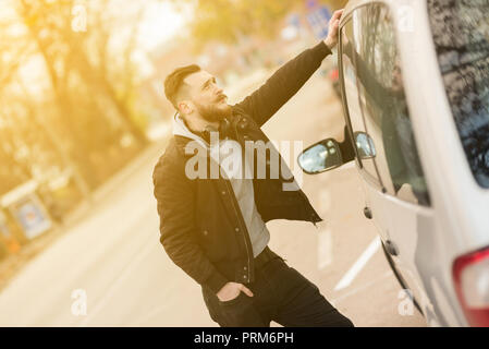 A handsome young hipster man standing next to his car and waiting. Stock Photo